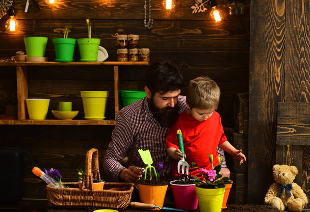 happy gardeners with spring flowers. Family day. Greenhouse. bearded man and little boy child love nature. Father and son. Fathers day. Flower care watering. Soil fertilizers. Fertile present - Фото, зображення