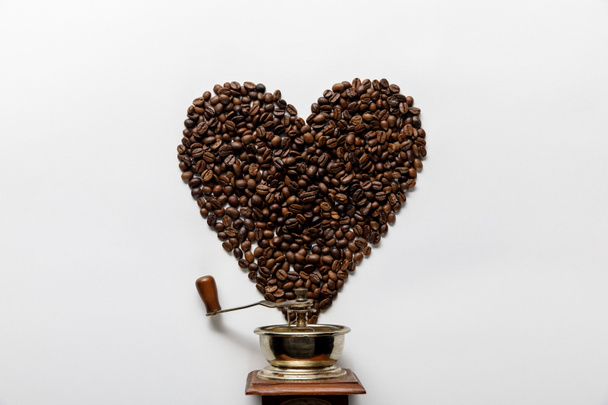白い背景にヴィンテージコーヒーグラインダーの近くにコーヒー粒で作られた心のトップビュー - 写真・画像