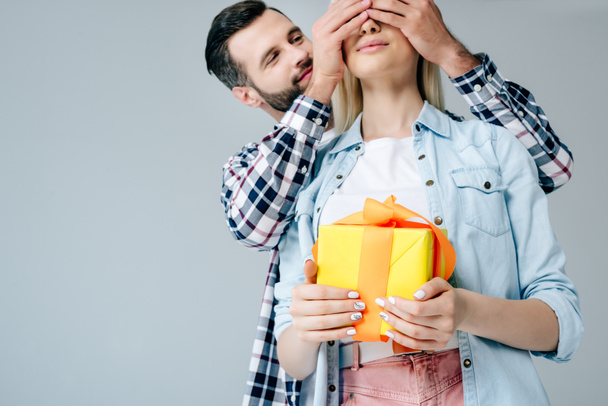 handsome man Covering Eyes of girl holding present isolated on grey - Foto, immagini