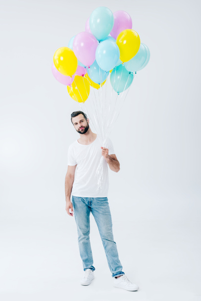 man in casual clothes holding colorful balloons on grey and looking at camera - Фото, изображение