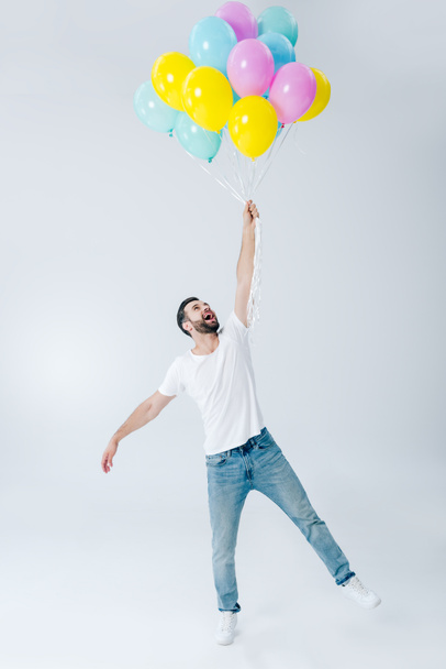 ενθουσιασμένος άνθρωπος σε casual ρούχα κρατώντας πολύχρωμα μπαλόνια σε γκρι - Φωτογραφία, εικόνα