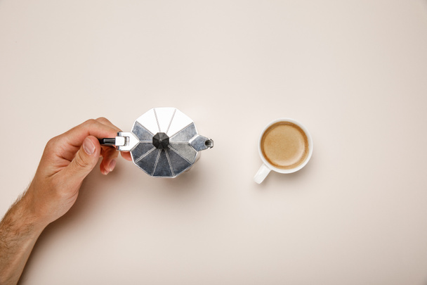 vágott kilátás az ember gazdaság fém kávé pot közelében kávéscsésze bézs alapon - Fotó, kép