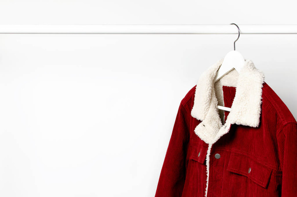 Red corduroy men's jacket on white coat hanger on rod against light wall flat lay copy space. Male fashion, autumn spring coat, youth hipster clothes stylish thing denim trendy jacket, store sale - Photo, Image