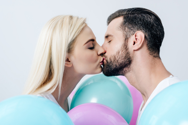 krásný pár líbání poblíž balónků izolovaných na bílém - Fotografie, Obrázek