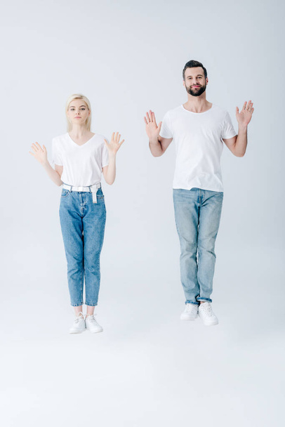 man and young woman jumping with open palms on grey - Foto, afbeelding