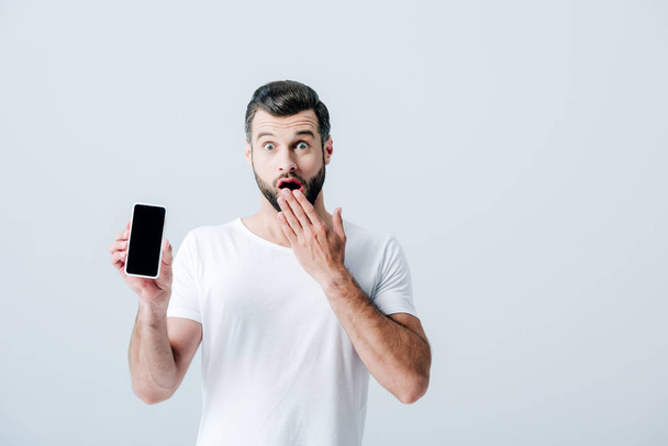 shocked man covering mouth and showing smartphone with blank screen isolated on grey - Foto, afbeelding