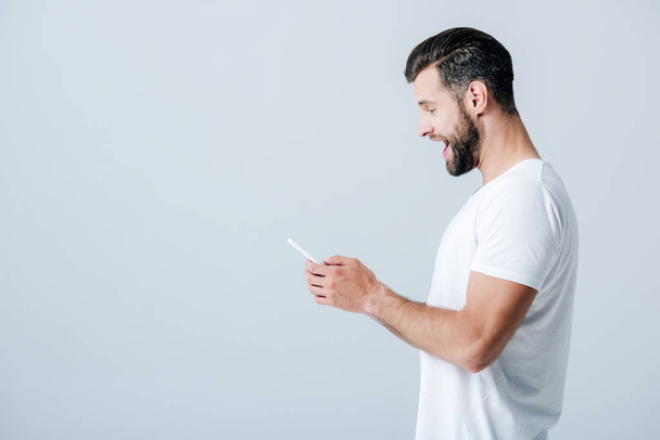 side view of excited man using smartphone isolated on grey - Photo, Image