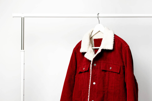 Red corduroy men's jacket on white coat hanger on rod against light wall flat lay copy space. Male fashion, autumn spring coat, youth hipster clothes stylish thing denim trendy jacket, store sale - Photo, Image
