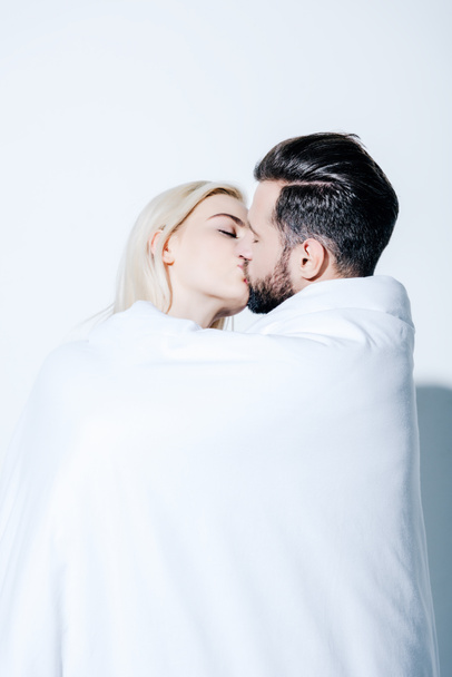 beautiful couple with closed eyes covered in blanket kissing on white - Zdjęcie, obraz