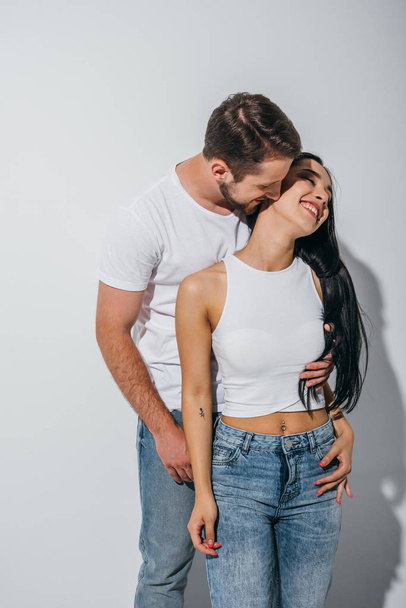 young man hugging girlfriend while girl smiling and looking away - Foto, imagen