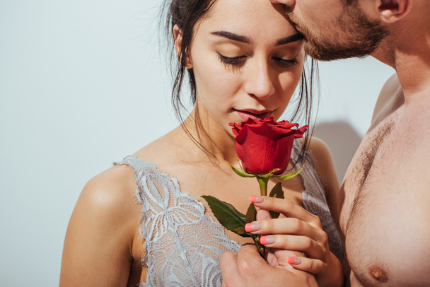 handsome naked man kissing girlfriend in forehead while girl sniffing red rose - Foto, afbeelding