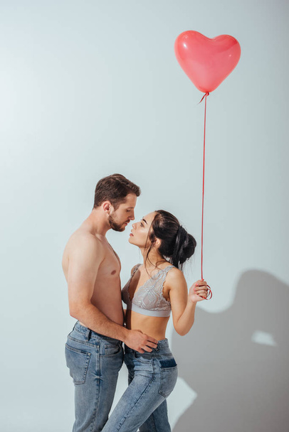 сексуальная пара обнимается и пытается поцеловаться, пока девушка держит воздушный шар в форме сердца
 - Фото, изображение