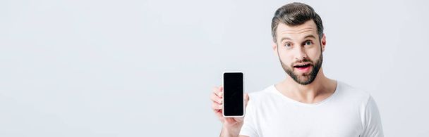 plano panorámico del hombre sorprendido mostrando teléfono inteligente con pantalla en blanco aislado en gris
 - Foto, imagen