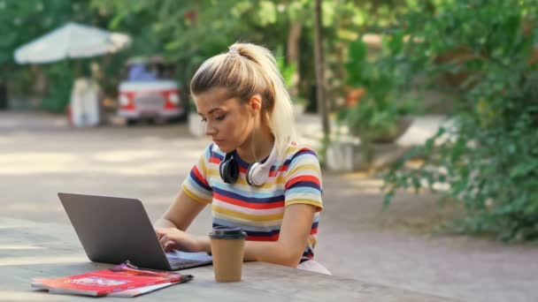 Koncentrovaná hezká studentka používající přenosný počítač při sezení v kavárně venku - Záběry, video