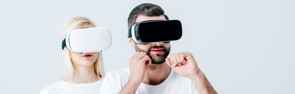 panoramic shot of man with clenched fists and girl in Virtual reality headsets isolated on grey - Photo, Image