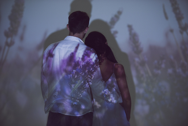 back view of girl and man hugging while standing in darkness on light of projector - Photo, Image