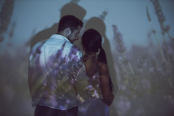 Rückansicht von Mädchen und Mann, die sich umarmen und einander anschauen, während sie an einem dunklen Ort stehen  - Foto, Bild