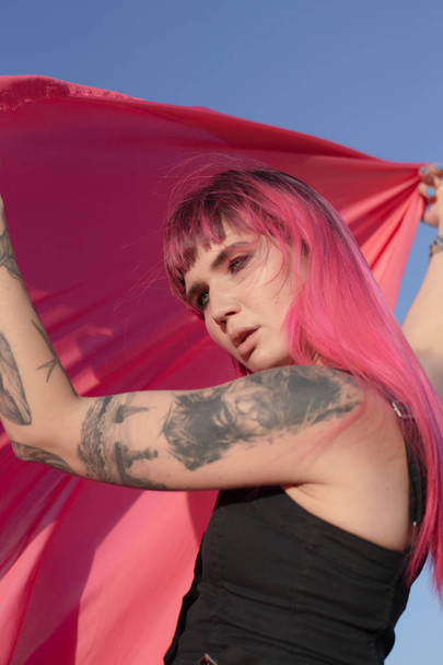 Giovane donna dai capelli rosa con pezzi di panno rosa danza vicino al campo con generatori di vento. Mulino a vento al tramonto. Ritratto di moda
 - Foto, immagini