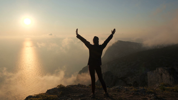 Silhuette Young Mujer brazos extendidos observando una hermosa puesta de sol dramática sobre un mar de una alta montaña en Crimea
. - Metraje, vídeo