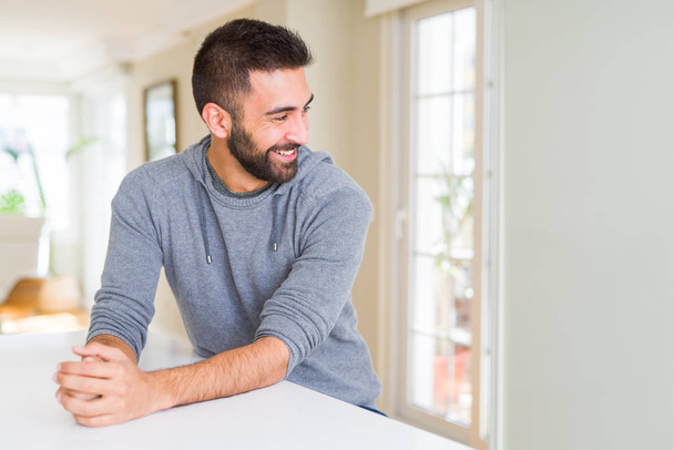 Handsome hispanic man wearing casual sweatshirt at home looking away to side with smile on face, natural expression. Laughing confident. - Photo, Image
