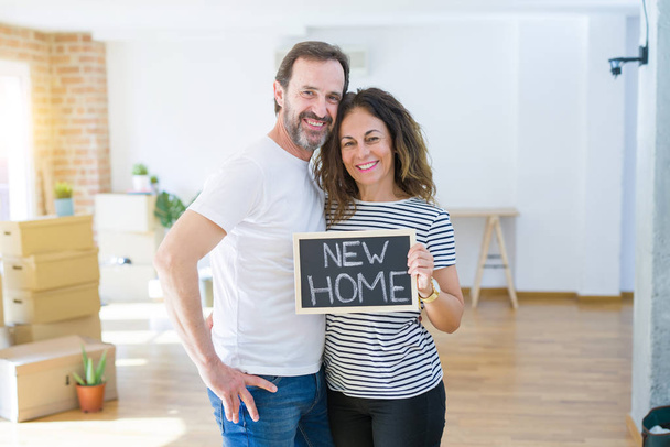 新しい家に引っ越す中年のシニアカップル、新しいホームテキストで黒板を持つアパートマントと恋に幸せそうに微笑む - 写真・画像