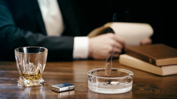vista parcial do empresário sentado à mesa com charuto e cinzeiro, isqueiro e copo de uísque e papéis de fixação
 - Filmagem, Vídeo