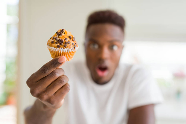 Afro-amerikai ember eszik csokoládé chips Muffin félek sokk egy meglepetés arc, fél és izgatott a félelem kifejezése - Fotó, kép