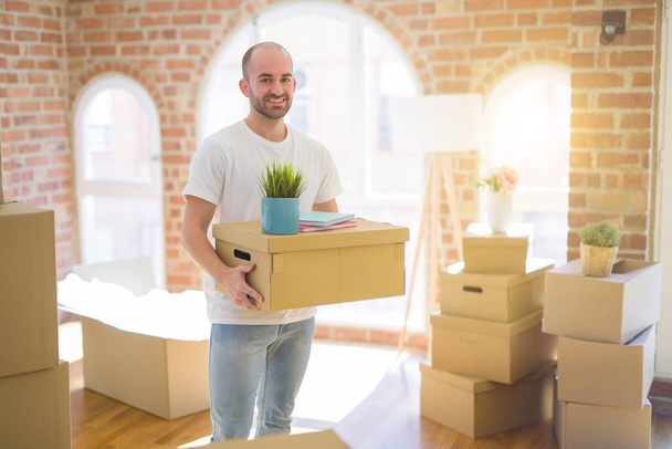 Молодой красивый мужчина переезжает в новый дом, держа в руках картонные коробки смайлик
 - Фото, изображение