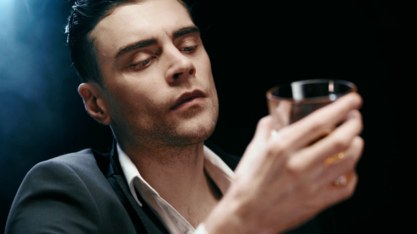 selective focus of pensive businessman shaking glass and drinking whiskey on black - Filmmaterial, Video
