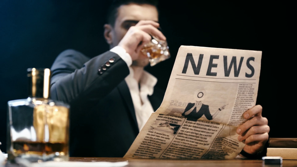 selektivní zaměření obchodníka čtení novin a pití whiskey u stolu na černém - Záběry, video