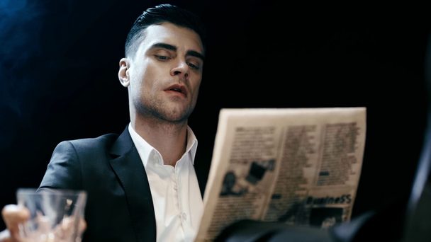 focused businessman reading newspaper and drinking whiskey on black - Materiaali, video
