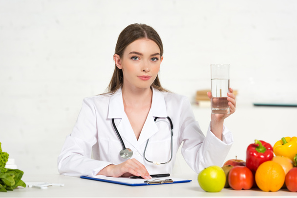 dietetikus fehér kabátot gazdaság pohár vizet a munkahelyen - Fotó, kép