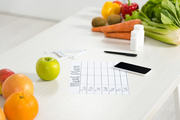 meal plan, smartphone with blank screen, pills, pen, caliper, fresh fruits and vegetables on table - Photo, Image