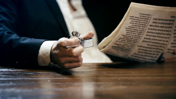 κομμένη θέα του επιχειρηματία που κάθεται σε ξύλινο τραπέζι, διαβάζοντας εφημερίδα και κρατώντας αναπτήρα - Πλάνα, βίντεο