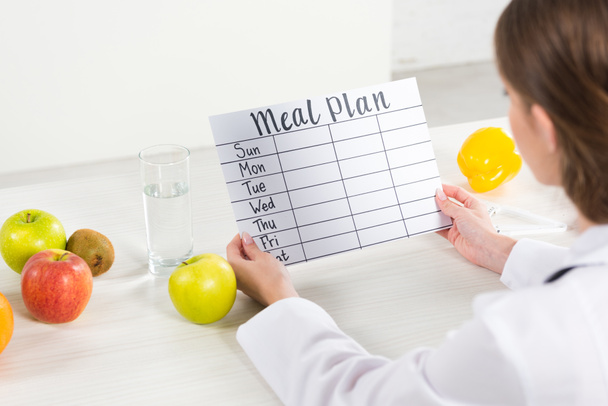 cropped view of dietitian in white coat holding meal plan at workplace - Photo, Image