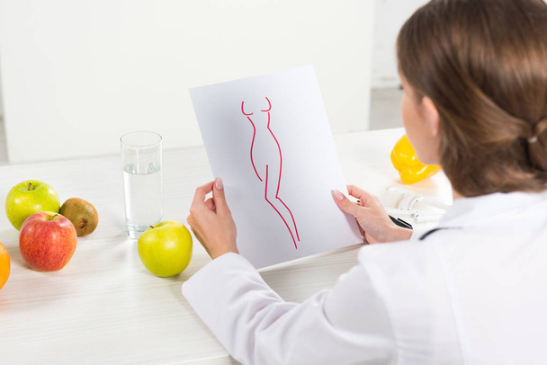 cropped view of dietitian in white coat holding paper with perfect body image at workplace - Foto, Bild
