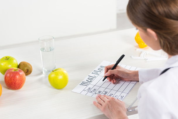 cropped view of dietitian writing meal plan at table - Zdjęcie, obraz