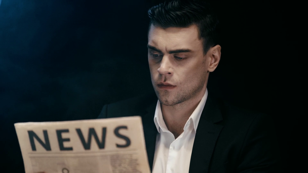 geconcentreerde zakenman zittend aan tafel met asbak, lees krant en whisky drinken op zwart in rook - Video