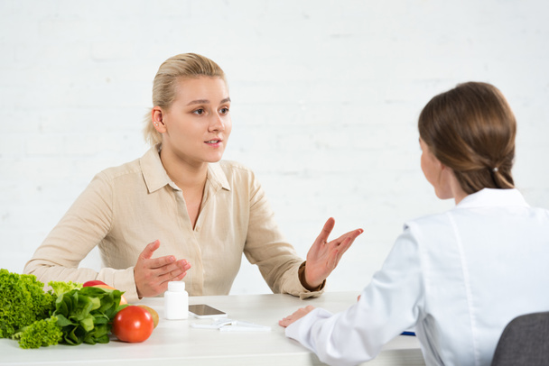 paciente e nutricionista em casaco branco à mesa com legumes frescos
 - Foto, Imagem