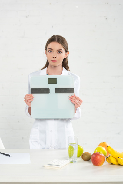 vista frontal del dietista en bata blanca sosteniendo balanzas digitales
 - Foto, imagen