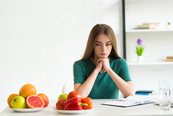 sad woman sitting at table with fresh fruits and vegetables - Фото, изображение