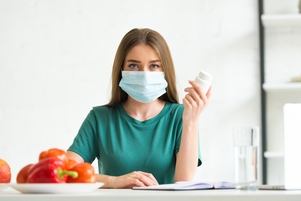 front view of woman in medical mask holding pills - Foto, imagen