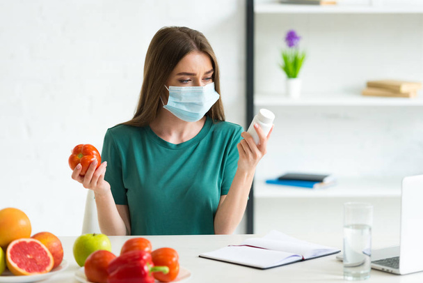 young woman in medical mask holding tomato and pills at home - Foto, imagen