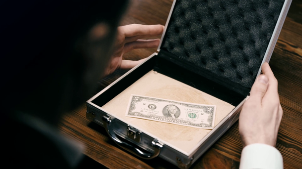 περικομμένη θέα του επιχειρηματία που ανοίγει τον χαρτοφύλακα με τραπεζογραμμάτιο δολαρίου σε ξύλινη επιφάνεια - Πλάνα, βίντεο