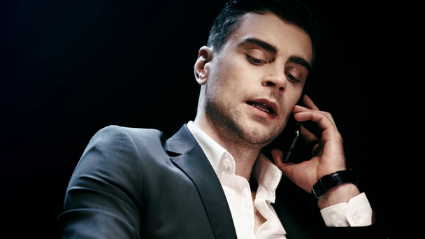 confident businessman in wristwatch talking on smartphone and blinking on black - Footage, Video