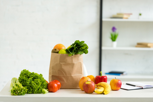 paper bag with fresh fruits and vegetables and textbook with pen on table - Foto, Bild
