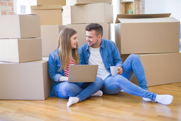 Young couple sitting on the floor around cardboard boxes using c - Photo, Image