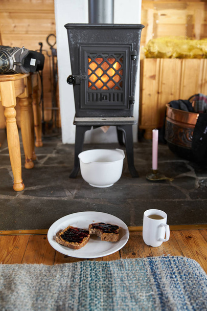 Sentada frente a un fuego en una estufa de leña con tostadas y té
. - Foto, Imagen