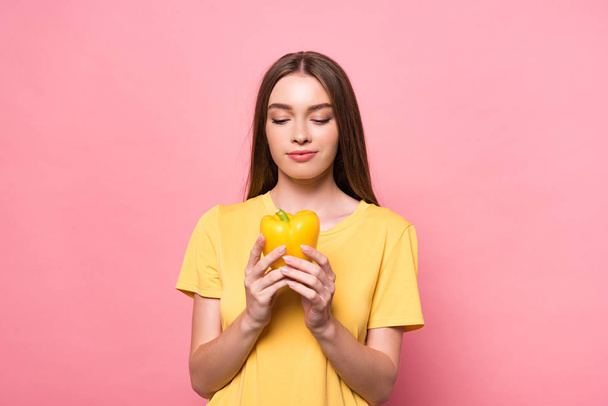 front view of attractive young woman in t-shirt holding yellow bell pepper on pink - Zdjęcie, obraz