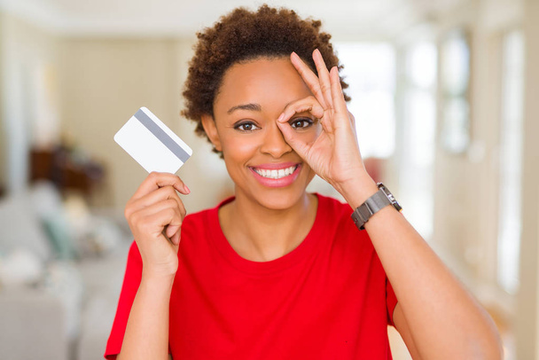 Kredi kartı ile ok işareti ile el parmaklarının arasından seyir göze yapıyor gülümseyen mutlu yüz tutan genç Afro-Amerikan kadın - Fotoğraf, Görsel